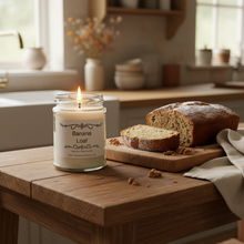 Load image into Gallery viewer, A jar candle labeled 'Banana Loaf' by Karmen's Tear Room, made from pure soy wax, sitting on a wooden surface against a corkboard background.