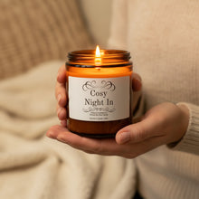 Load image into Gallery viewer, Hand holding a lit candle labeled 'Cosy Night In' against a soft background