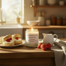 Load image into Gallery viewer, A glass jar candle labeled 'Strawberries &amp; Cream' sits on a wooden table in a warm kitchen setting, styled with strawberry scones, fresh strawberries, and a small white pitcher.