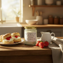 Load image into Gallery viewer, A glass jar candle with a gold metal lid and a white label reading 'Strawberries &amp; Cream' on a wooden surface against a corkboard background.